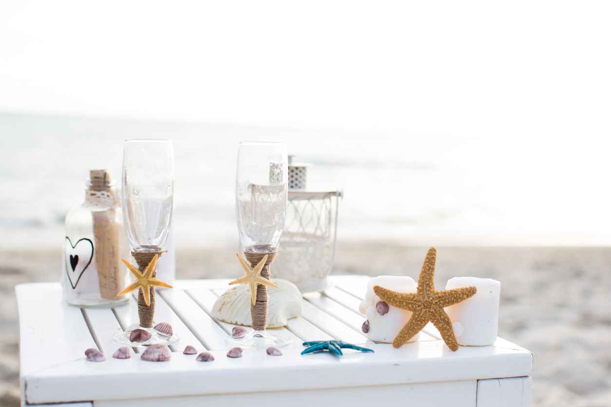 Romantic wedding decoration for a beach wedding including seashells, starfish, glasses, and letters in a bottle.