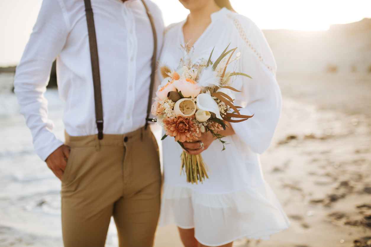 A closeup of a couple getting married on the beach; focus of their rustic bouquet