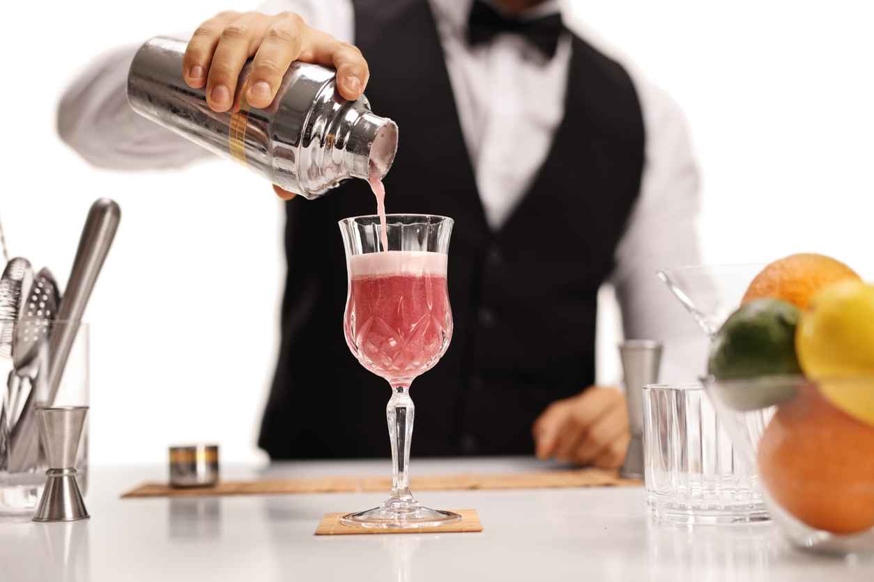 Bartender pouring his signature cocktail in a glass isolated on white background